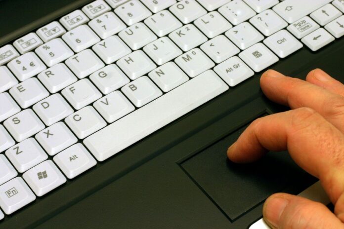 A man fingers using a mouse pad on a lap top computer